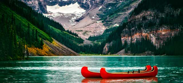 Fotografía de un lago de Canadá con dos canoas rojas y las montañas de fondo